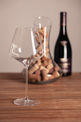 Crystal shiny glass, bottle of red wine, transparent decanter filled with corks on wooden table. Closeup, vertical, selective focus, a side view. Concept degustation in winery cellar