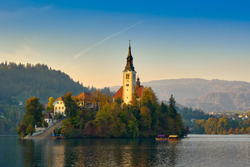 Beautiful church in middle of slovenian Bled lake surrounded by mountains on evening day with blue skies in Bled, Slovenia. Travel landmarks and landscapes concept