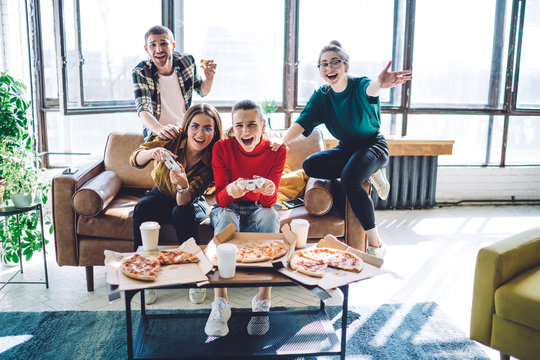 Excited people on couch trying to win in video game and eating pizza