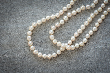 White natural pearl necklace laid on grey rough rock textured tile.