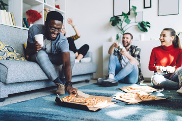 African American man taking piece of pizza while having fun with friends