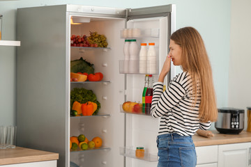 Woman feeling bad smell from fridge in kitchen - obrazy, fototapety, plakaty