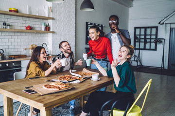 Young joyful groupmates chortling together with eat and drink at home