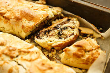 Two rolls with raisin and nuts on a pan and baking paper and a cut piece of roll