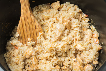 Ready pilaf with crumbly rice and wooden spoon after cooking in slow cooker.