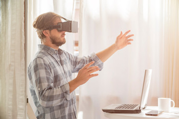  Young bearded man wearing virtual reality glasses in modern interior,    blurred background. Handsome caucasian male using VR headset, playing   video games.