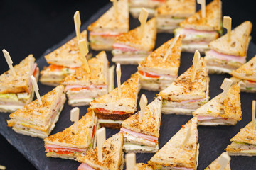Quick snacks, canapes, mini sandwiches with ham, tuna, vegetables and cheese. Triangular bread on a rack for guests and participants of the event. Catering, event services. Service