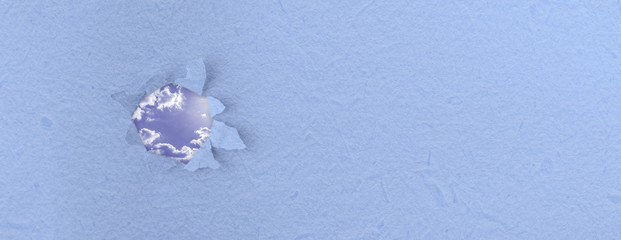 a blank piece of torn paper with a hole in it and the cloudy sky behing it