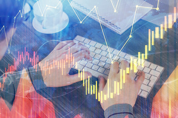 Double exposure of graph with man typing on computer in office on background. Concept of hard work.