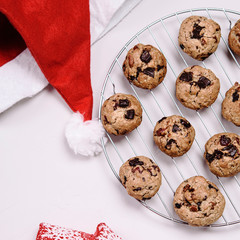Christmas cherry, cinnamon and chocolate oatmeal cookies and Santa hat on white background. Treat for Santa Claus. Selective focus