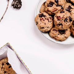 Christmas cherry, chocolate and pecans oatmeal cookies and gift box  with cookies on grey  background decorated fir cones. Delicious gift. Hygge. Selective focus