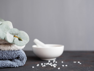Fototapeta na wymiar Wellness und Spa, Handtücher und eine Schüssel mit Badesalz auf einem grauen Hintergrund