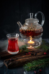 A glass of hot herbal tea with black currants in a teapot on a dark wooden background. Natural forest drink with vitamins
