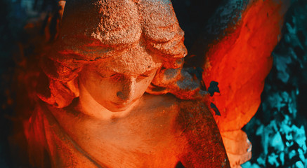 Beautiful angel on a cemetery against the background of leaves. Fragment of ancient statue.