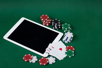 playing chips, four aces and a tablet on a green background