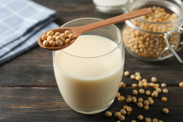 Glass of soy milk, soybeans seeds on spoon, napkin on wooden background, space for text. Closeup