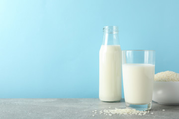 Bottle of rice milk, glass of rice milk, rice plate on grey table again blue background, space for text