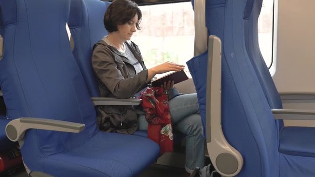 at the window of a moving train sits Caucasian a middle aged woman brunette with short hair in a black jacket Reading a book leafing through the pages side View