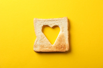 Toast bread with shape of heart on yellow background, top view
