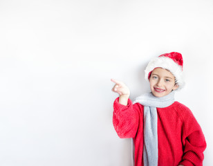 7 years old smiling child in santa hat, red pullover and gray scarf with showing with one finger on left part of picture with space for text there. One, isolated, display