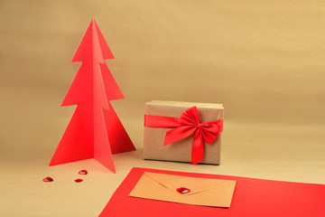 Gift box and envelope with red wodden Christmas tree on a natural brown background with scattered hearts.