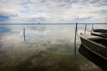 Old metal fishing boats at calm lake in cloudy day. Horizon line and reflection in water