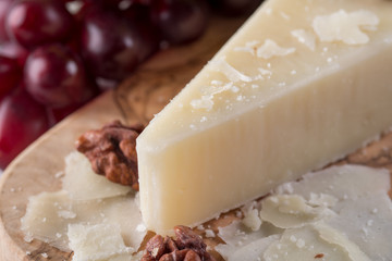 Pecorino romano, hard italian sheep milk cheese on wooden cutting board with grape, selective focus