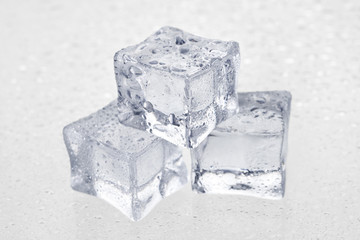 Three ice cubes, in drops, on a white background.