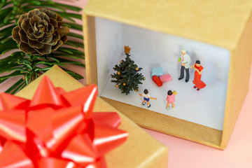 A miniature family is celebrating christmas in a gift box with a little christmas tree and presents for the children