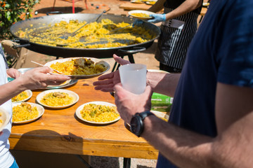  person delivering a plate of paella with cook making a paella