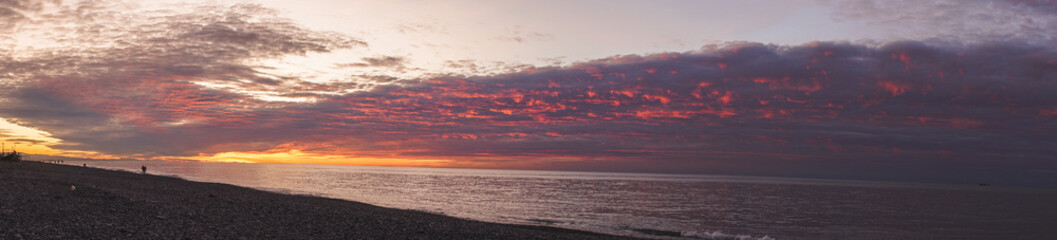 Sea sunset with pebble beach. The sun reflects on water, waves and stones creating a beautiful reflection. Beautiful sky and clouds