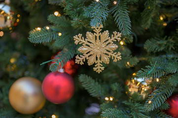 Golden snowflake Christmas decoration between Christmas balls and lights in a Christmas tree.