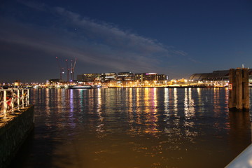 Fototapeta premium Romantic autumnal evening panorama over the canal waters of the Dutch metropolitan city of Amsterdam, among the lights and illuminations of the buildings and skyscrapers