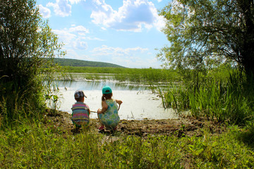 Little brother and sister olaying near the river, back view. People, family, nature concept. Kids outdoors. 