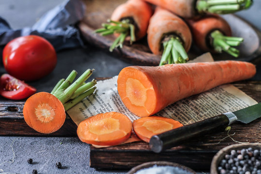Photo of Fresh Carrots On Wooden Cutting Board. On wooden Dark Background. Slice of carrots with green leaves. Carrot around vegetables, salt, black pepper, corn, broccoli. Drops of water. Image.