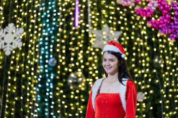 Portrait of a cheerful Asian woman wears Santa Claus costume presents gift for the Christmas festival and new year celebration with beautiful bokeh light background.