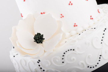 White wedding cake closeup with icing flower and black and red accents