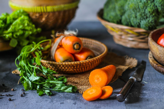 Photo of Fresh Carrots On A Plate. On wooden dark background. Bunch of fresh carrots with green leaves on Wooden Cutting Board. Carrot around vegetables, salt, black pepper, corn, broccoli. Image