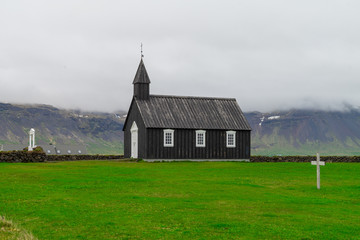 Fototapeta na wymiar Black Church. Attraction In Iceland. Stylish Church with a tower in a green field. Journey around the island. The Landscape Of Iceland. Tourism.