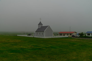 White Church in fog. Attraction In Iceland. Stylish Church with a tower in a green field. Journey around the island. The Landscape Of Iceland. Tourism.