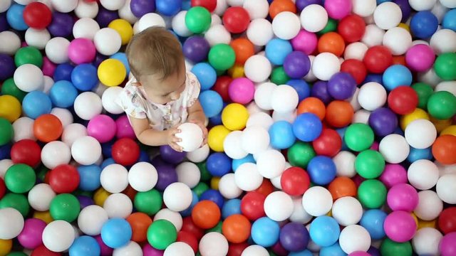 One year infant baby on the playground. plays with colorful plastic balls in a special pool. top view