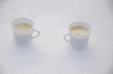 Winter. December. Against the background of white fluffy snow, there are two white cups of freshly brewed aromatic coffee.