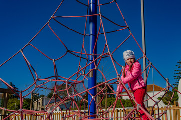Little girl on a playground climbs upstairs. Child playing outdoors in spring. Happy kid in kindergarten or preschool