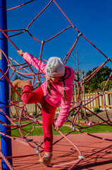 Little girl on a playground climbs upstairs. Child playing outdoors in spring. Happy kid in kindergarten or preschool