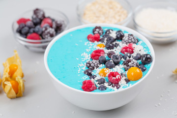 Breakfast smoothie bowl with blue spirulina, yogurt, raspberries, blueberries, Blackberries, physalis and coconut flakes. Detox smoothie bowl. Vegan food.