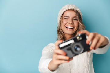 Portrait of nice cheerful woman winking and taking photo on retro camera