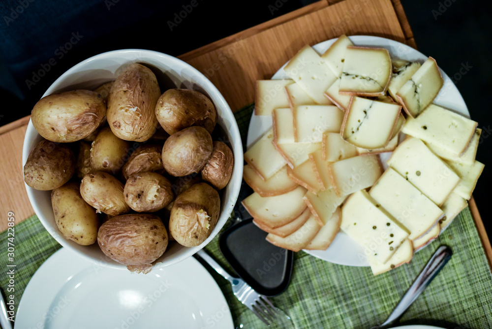 Wall mural close up on slices of cheese and potatoes at raclette party