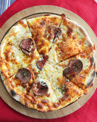 pizza on a round wooden Board top photo. Pizza with cheese and salami on a a wooden Board.