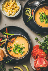 Flat-lay of Turkish traditional lentil soup Mercimek in bowls with parsley, vegetable, flatbread, pickled peppers over concrete background, top view, close-up. Vegan, Oriental, Middle Eastern cuisine