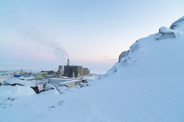 Winter industrial landscape with a snowy mountain slope and thermal power plant. Energy and ecology of the Arctic. Power station in the far North of Russia. Anadyr, Chukotka, Siberia. Cold weather.